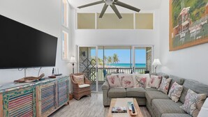 Sala de estar com uma TV grande, sofá, poltrona e varanda com vista para a praia.