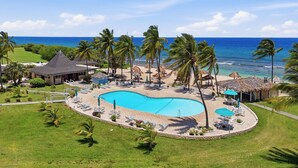 Um resort com piscina, palmeiras e vista para o oceano.