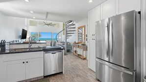 Uma cozinha moderna com eletrodomésticos de aço inoxidável, armários brancos e uma escada em espiral que dá acesso a um andar superior.