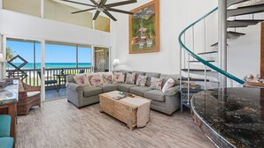 Uma sala de estar moderna com um amplo sofá em forma de L, uma mesa de centro de madeira e uma mesa de jantar com tampo de vidro. Uma escada em espiral com corrimão de vidro é visível à direita.