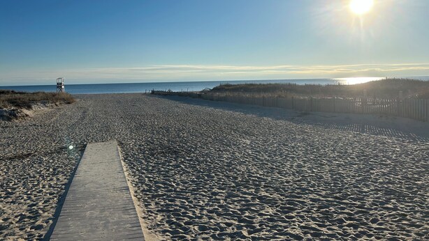 A beach with a wooden walkway leading to the water, a lifeguard tower, and a fence along the dunes. - Cozy condo in downtown Harwich Port short walk to Bank Street Beach (Harwich)