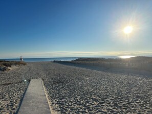 Une plage avec une promenade en bois menant à l’eau, un poste de surveillance pour les sauveteurs et une clôture le long des dunes.