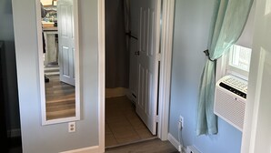 A hallway with a wooden floor, a door leading to a bathroom, a mirror on the wall, and a window with curtains. - Cozy condo in downtown Harwich Port short walk to Bank Street Beach (Harwich)