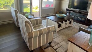 A living room with a TV, a coffee table, striped armchairs, and a view of the outdoors. - Edgewater #4 Moose (Polson)