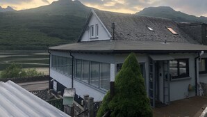 Een huis met een schuin dak, grote ramen en uitzicht op bergen en een meer.