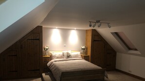 Een slaapkamer met een schuine kap, houten wandbekleding, een bed met bloemenbeddengoed, twee nachtkastjes met bloevasen en een dakraam.