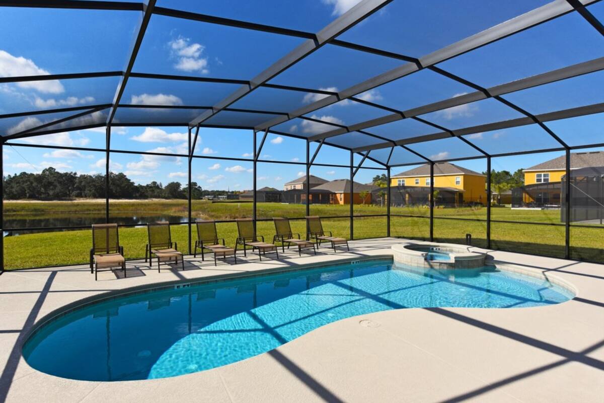 Una piscina cubierta al aire libre con sillones de descanso y un jacuzzi, rodeada por una valla metálica y con vistas a casas al fondo.