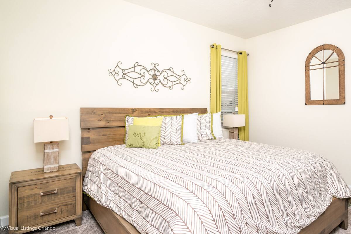 A bedroom with a wooden bed, a nightstand, a lamp, a mirror, and a decorative wall piece.