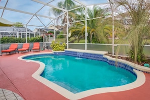 A pool with a blue tiled edge, surrounded by red lounge chairs and a glass-enclosed patio area with palm trees. - Highlands Reserve by Florida Star Vacations (Davenport)