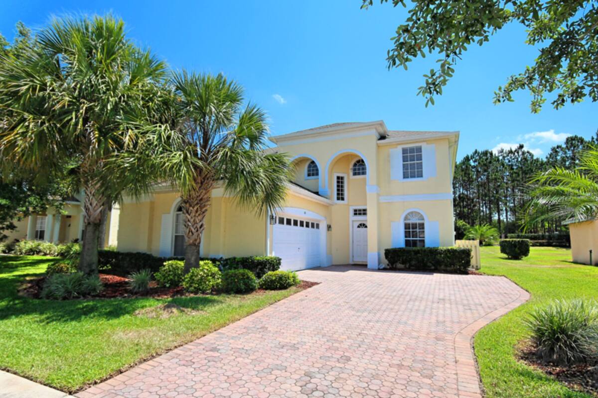 A two-story house with a driveway, palm trees, and a well-maintained lawn.