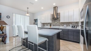 Una cocina moderna con una isla central, armarios blancos y un respaldo de piedra.