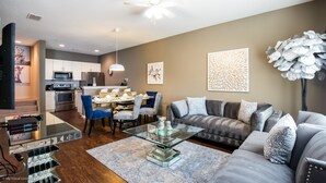 A modern living room with a glass coffee table, grey sofa, and a dining area with blue chairs. - West Lucaya Village Resort by Florida Star Vacations (Kissimmee)