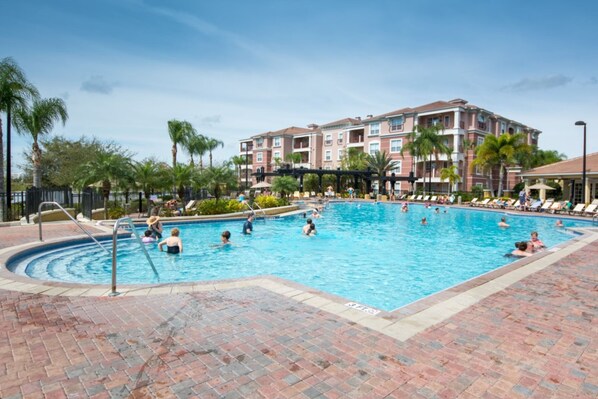 A swimming pool with people enjoying the water, surrounded by palm trees and a building with multiple balconies. - Vista Cay Resort by Florida Star Vacations (Orlando)