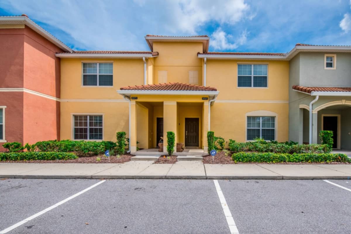 A row of townhouses with a central entrance, a parking lot, and a clear sky.