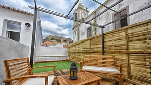 A rooftop terrace with wooden furniture, a lantern, and a view of a historic building in the background.