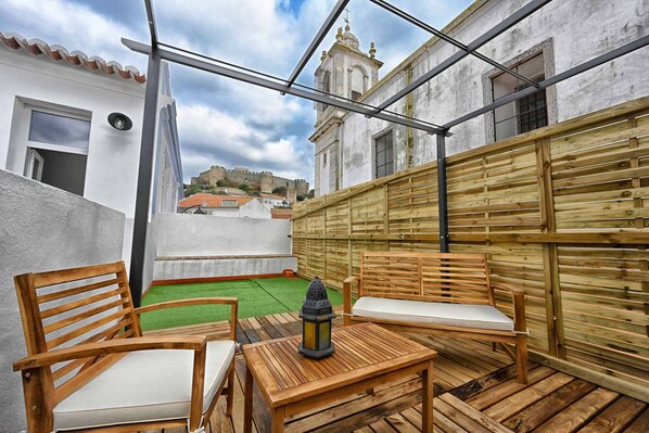Una terraza en la azotea con muebles de madera, un farol y vistas a un edificio histórico al fondo.