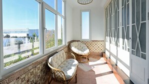 A sunlit room with large windows, two cushioned chairs, a hanging light fixture, and patterned walls.