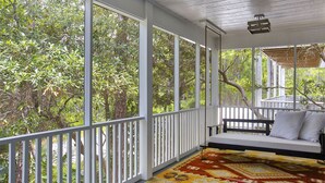 A covered porch with a white railing, a bench, and a patterned rug.