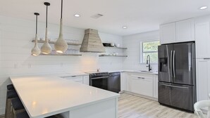 A modern kitchen with white cabinetry, a stainless steel refrigerator, a built-in oven, and pendant lights.