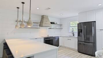 A modern kitchen with white cabinetry, a stainless steel refrigerator, a built-in oven, and pendant lights.