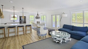 A modern kitchen with white cabinetry, a central island with stools, and a dining area with a glass table and blue sofa.