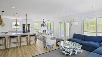 A modern kitchen with white cabinetry, a central island with stools, and a dining area with a glass table and blue sofa.