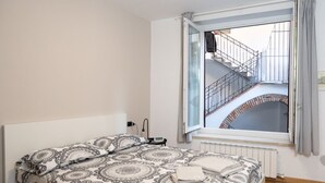 Una camera da letto con un letto grande, una finestra che mostra una scala e mattoni, e un termosifone sotto la finestra.