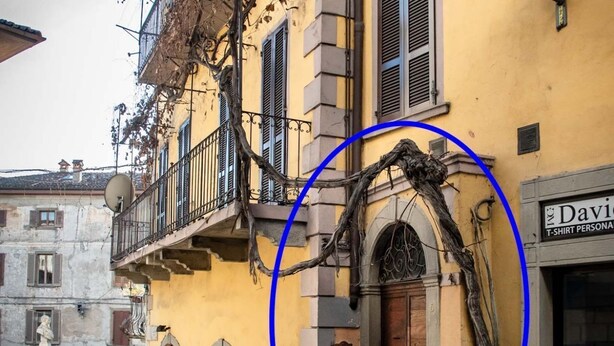 Un edificio giallo con un balcone, un portale ad arco e un cartello di negozio.