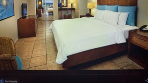 A hotel room with a large bed, a nightstand, a chair, and a desk. There is a door leading to a bathroom and a hallway. - 5 Star Aruba Resort Christmas week! (Noord)