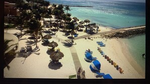 A beach resort with thatched-roof structures, lounge chairs, and a clear view of the ocean. - 5 Star Aruba Resort Christmas week! (Noord)