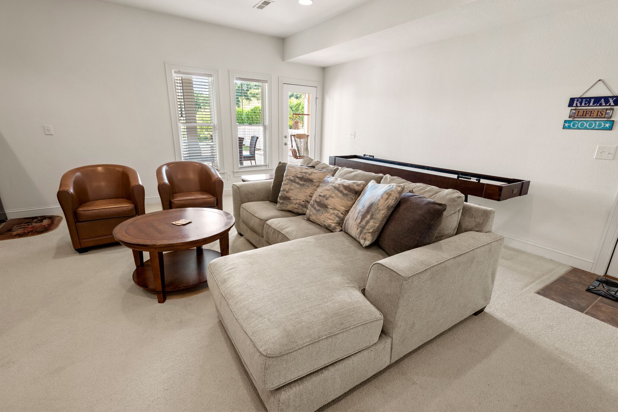 Un salon comprenant un canapé, deux fauteuils, une table basse et un téléviseur fixé au mur.