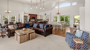 Ein geräumiges Wohnzimmer mit einer großen braunen Ledersofa, einem blau gemusterten Sofa und einem Couchtisch. Es gibt einen Essbereich mit einem Holztisch und Stühlen, und eine Küche im Hintergrund.