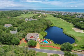 An aerial view of a residential area with a large house, a swimming pool, and a lake.