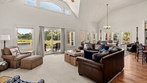Ein geräumiges Wohnzimmer mit hoher Decke, großen Fenstern und Blick ins Freie.