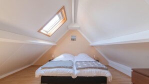 A bedroom with a sloped ceiling, a skylight, a bed with pillows, and a dresser. - Vissershuisje 09/04 with parking by Interhome (Bredene)