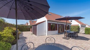 A patio area with a table and chairs, umbrellas, and a small building with a tiled roof. - Vissershuisje 09/04 with parking by Interhome (Bredene)