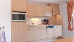 A compact kitchen with light wooden cabinets, a built-in microwave, a coffee maker, and a dishwasher. - Vissershuisje 09/04 with parking by Interhome (Bredene)