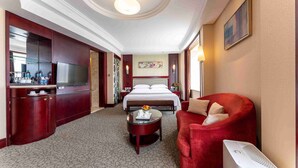 Een hotelkamer met een groot bed, een rode fauteuil, een tafeltje met een fruitschaal, een televisie en een minibar.