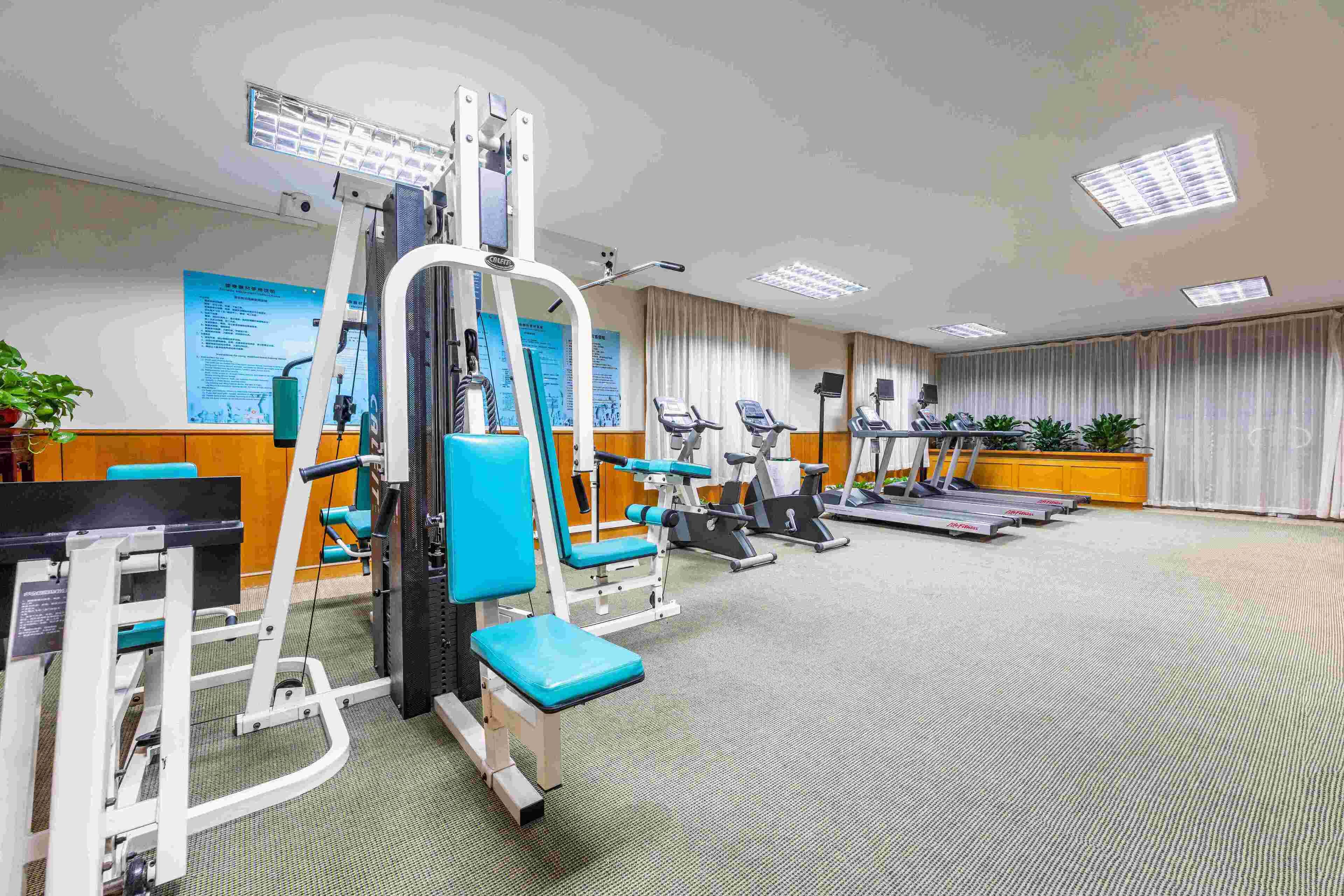 Un gimnasio con equipo de ejercicio, cintas de correr y suelo alfombrado.