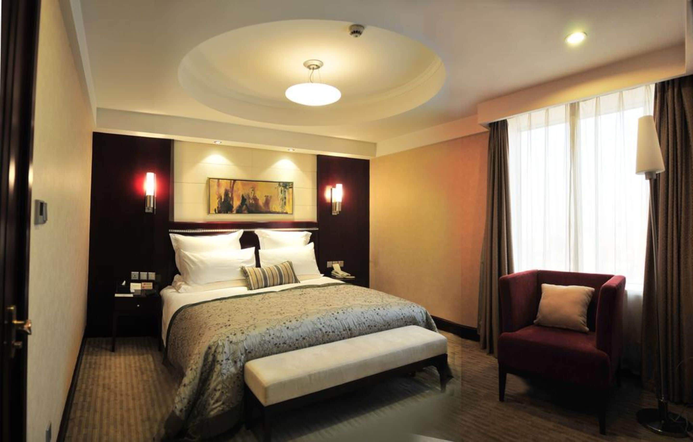 A hotel room with a large bed, a bedside table, a chair, and a painting on the wall.