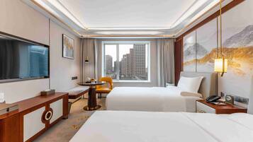 A hotel room with two beds, a desk, a chair, a TV, a window with a city view, and a painting on the wall.