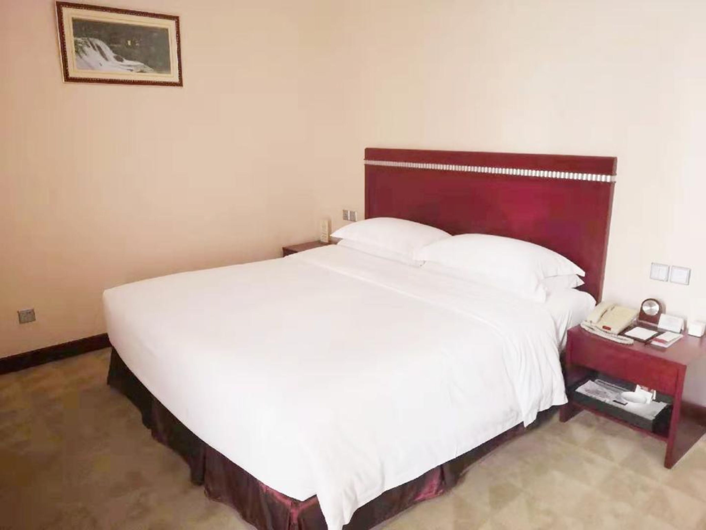 Une chambre d’hôtel avec un grand lit, une tête de lit en bois, une table de chevet avec un téléphone et un tableau encadré au mur.