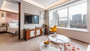 Een moderne hotelkamer met een bed, een televisie, een zithoek en een groot raam met uitzicht op de stad.