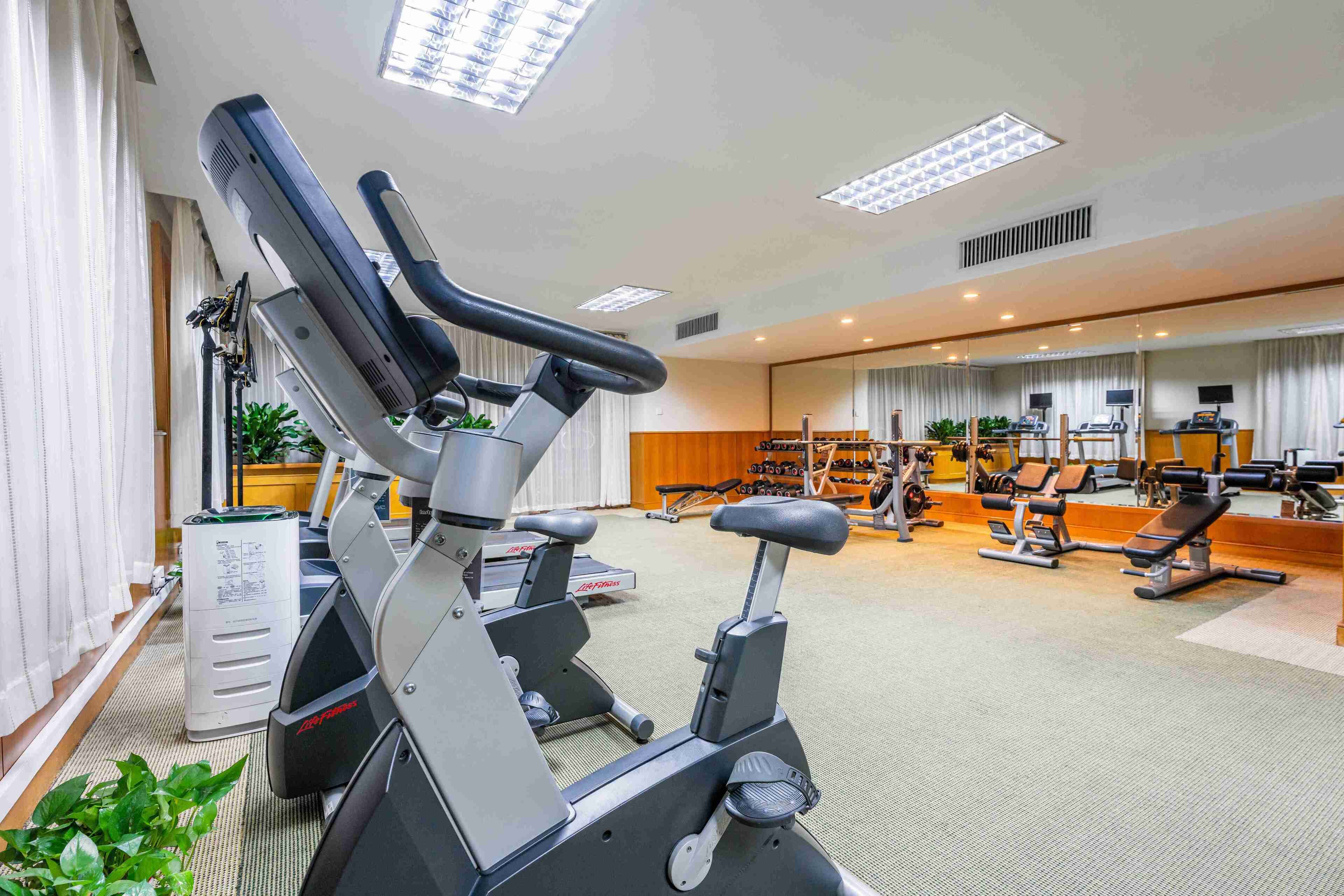 A gym with stationary bikes, weight machines, and a mirror wall.