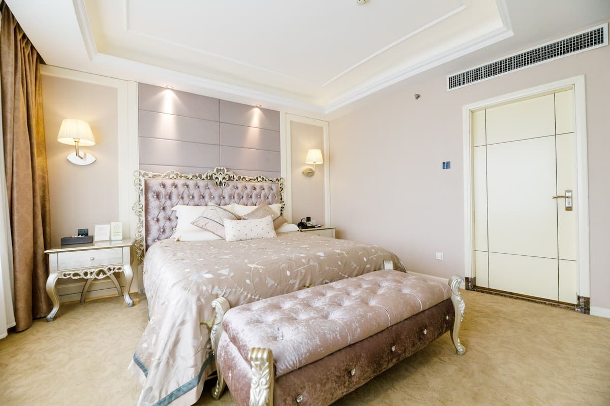 A spacious bedroom with a large bed, a nightstand, a bench, and a wardrobe.