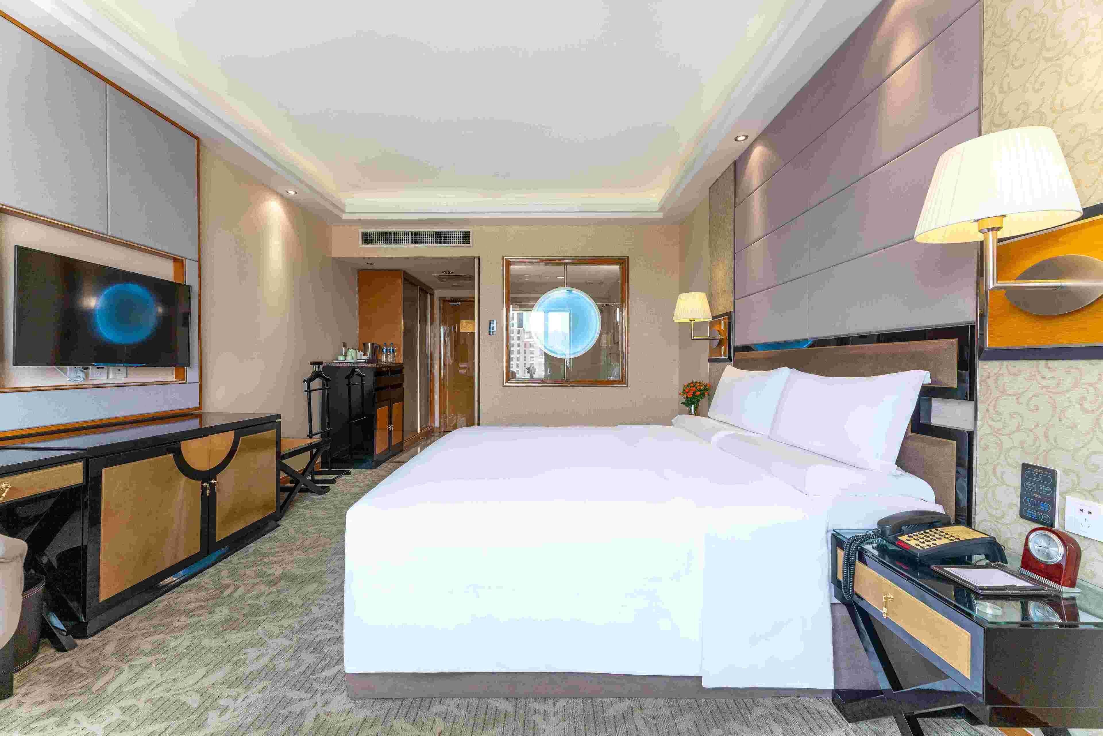 Une chambre d’hôtel avec un grand lit, un bureau avec une lampe, une télévision et un téléphone.
