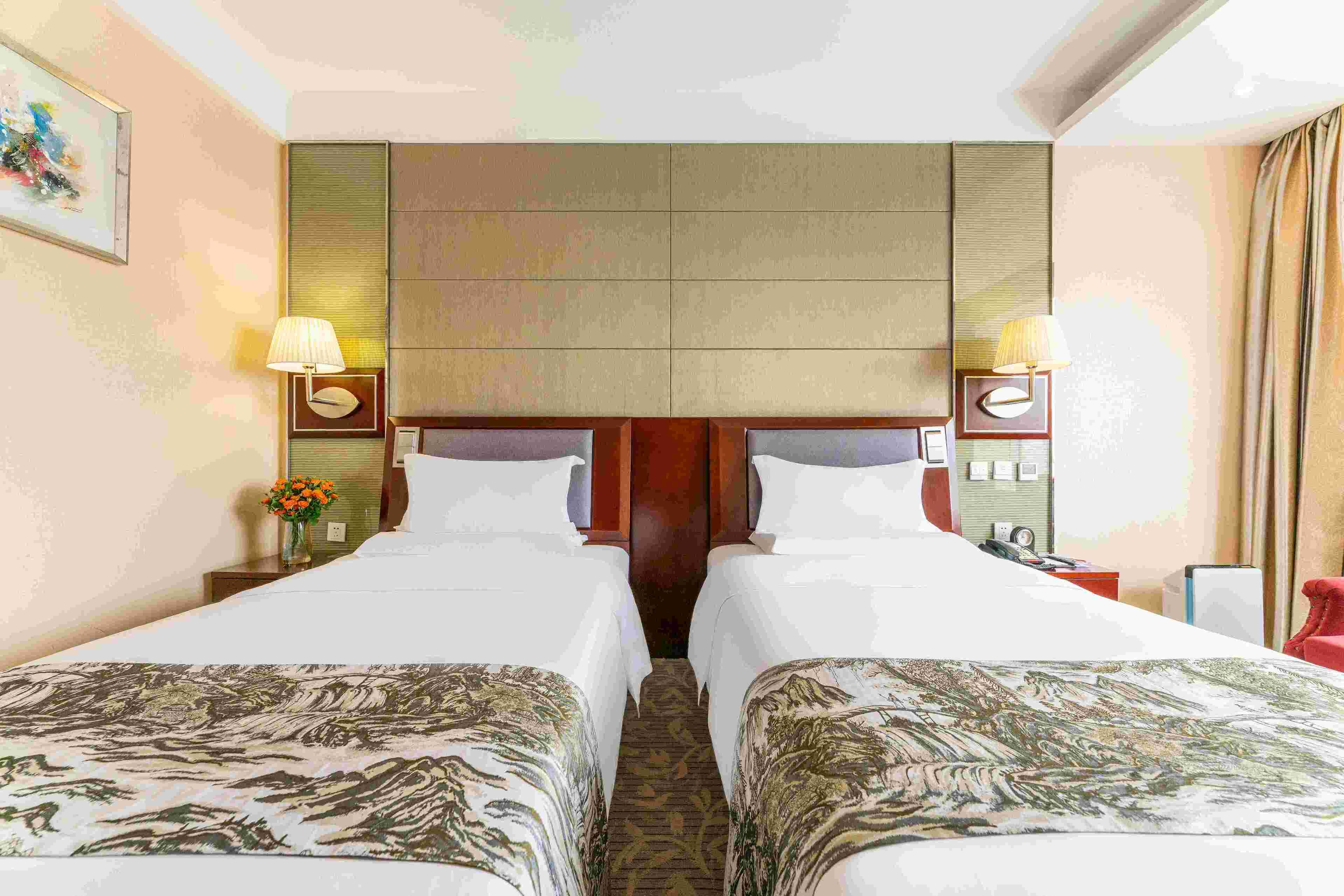 Une chambre d’hôtel avec deux lits, une tête de lit, des lampes de chevet, une table de chevet et un tableau au mur.