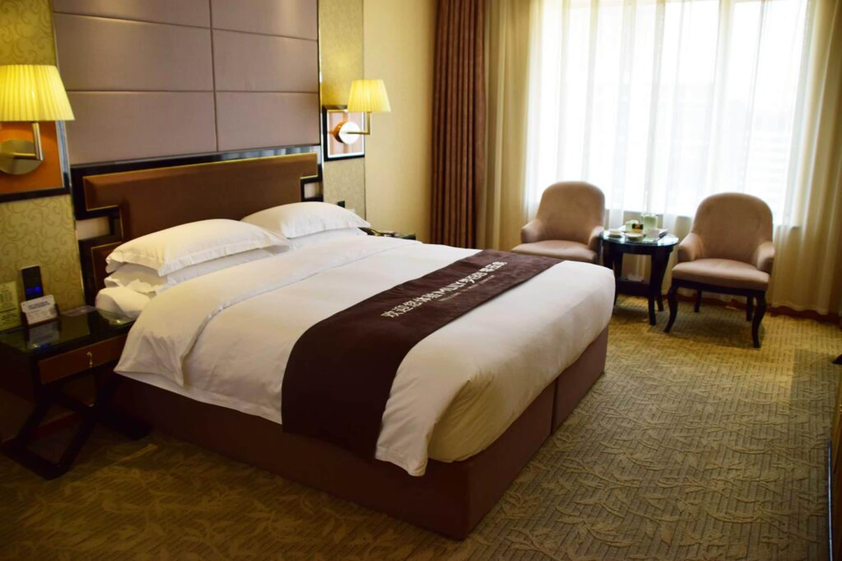 Habitación de hotel con una cama grande, dos sillones, una mesita y una lámpara.