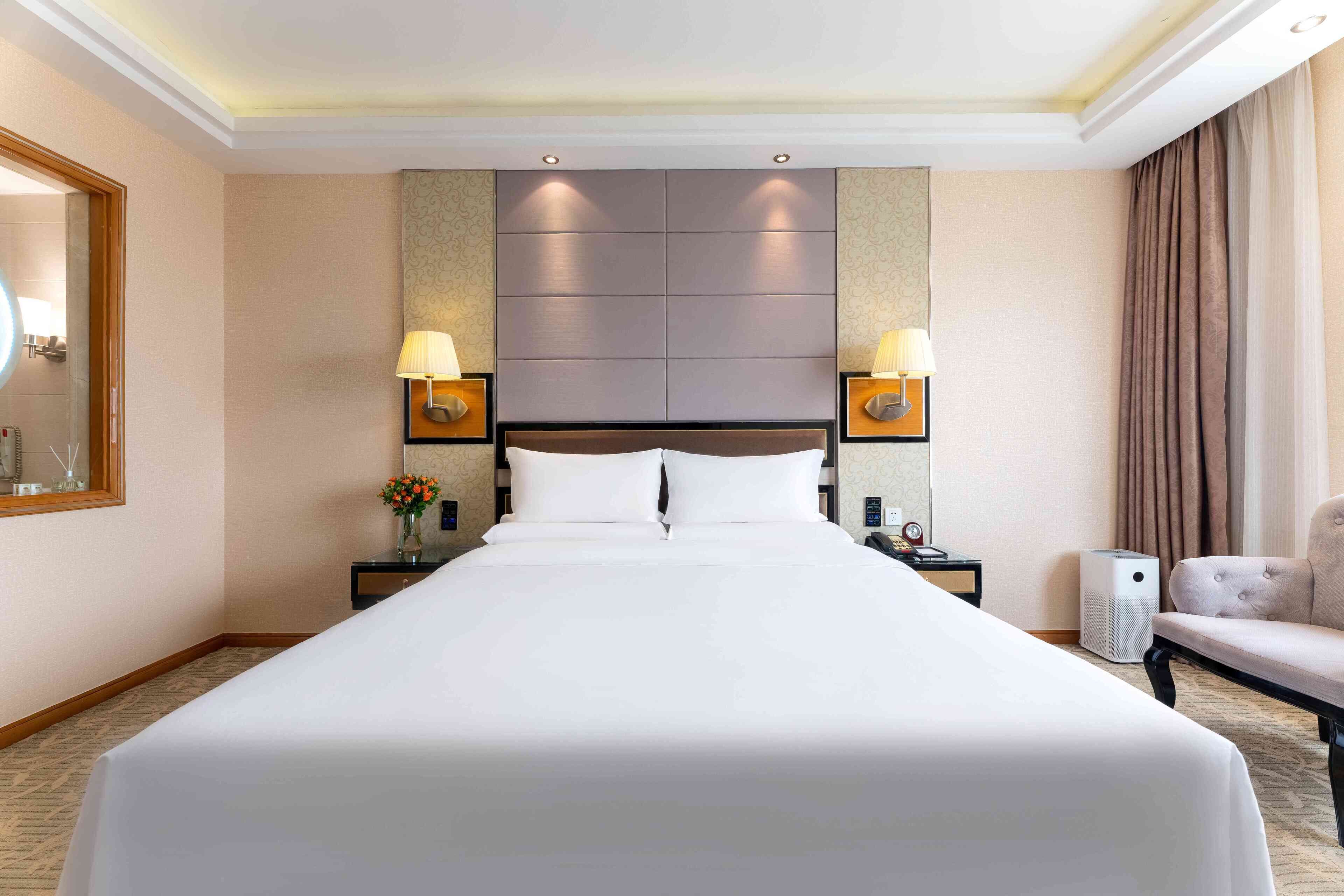 Une chambre d’hôtel avec un grand lit, deux lampes de chevet, une table de chevet, une chaise et un radiateur fixé au mur.