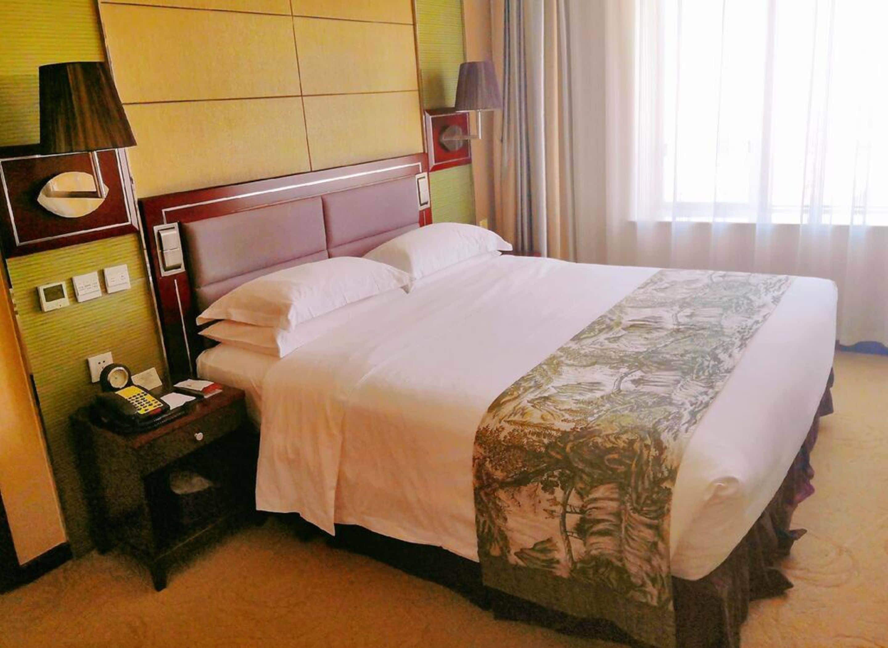 A hotel room with a bed, a nightstand, a lamp, and a mirror.